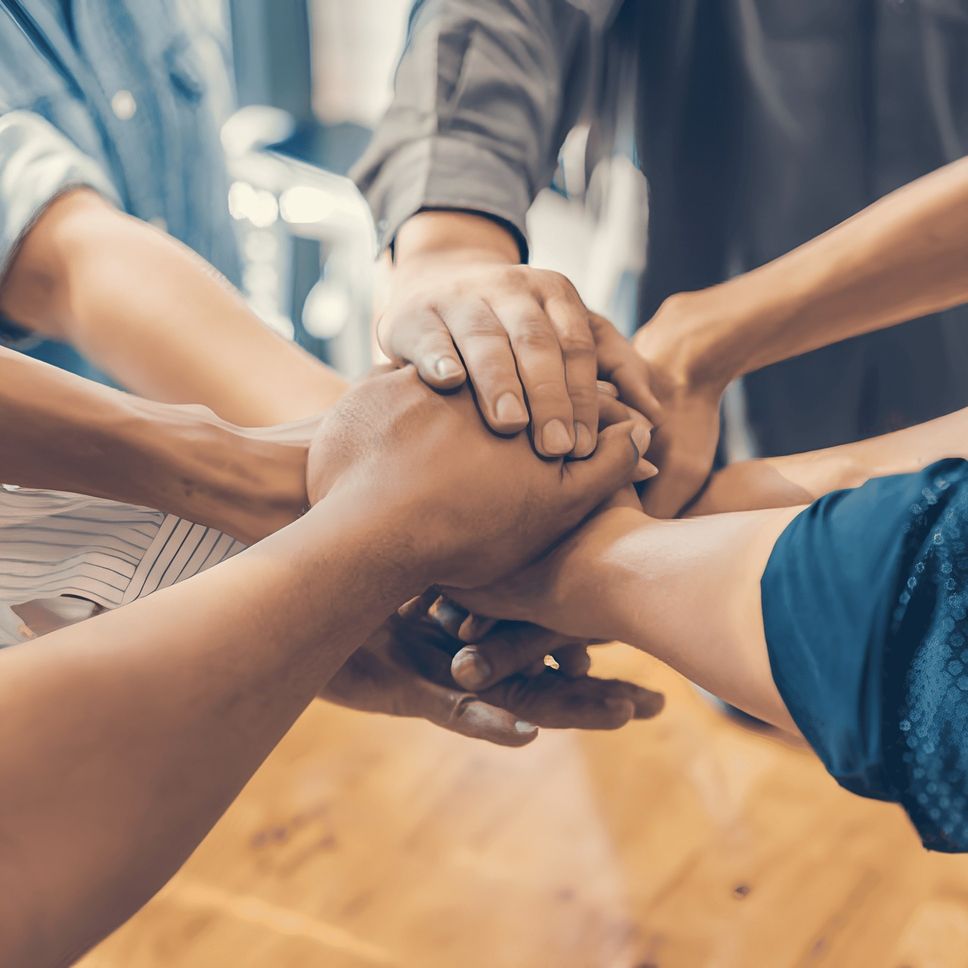 Eine Gruppe von Menschen legt ihre Hände zusammen, um Einheit und Zusammenarbeit zu symbolisieren